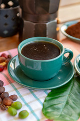 Cup with black coffee served outside with raw green, mature red and roasted coffee beans, decorated with green leaves from coffee plant