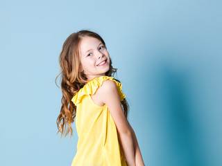 pretty, happy girl with brunette hair with yellow top posing in front of blue background and making different facial expressions