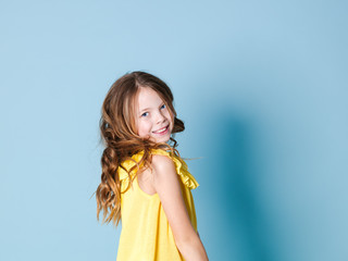 pretty, happy girl with brunette hair with yellow top posing in front of blue background and making different facial expressions
