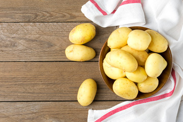 Young potatoes in a wooden bowl, napkin with red and white stripes on wooden table. Rustic style. Top view. Flat lay.