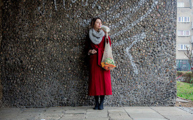 Style woman in red coat and net bag waking home after shopping.