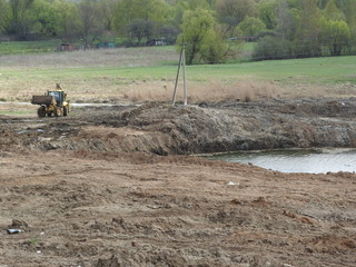 Tractor on the construction site against the river, trees and sky