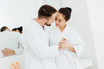 Obraz premium cheerful girl holding hands while looking at bearded boyfriend in bathroom