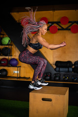 Fototapeta premium Fitness woman with afro braids jumping on box training at the gym, cross fit exercise. Female athlete doing box jumps