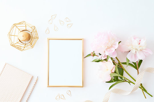 Flat lay composition with golden frame and light pink peonies on a white background