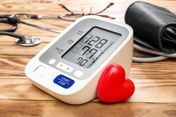 Blood pressure tonometer with red heart on wooden table. Medical concept.
