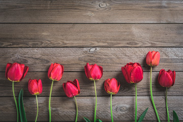 Fototapeta na wymiar Row of red tulips on wooden background with space for text, message. Mother's Day, Hello spring concept. Card. Flat lay. Top view. Rustic style. Toned. 