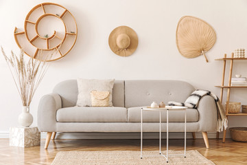 Stylish and cozy interior of living room with a lot of rattan accessories, design  gray sofa and wooden shelf. Korean style of home decor. Hanging rattan snail with airplants, hat and leaf. Template. 