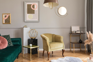 Stylish and luxury living room of apartment interior with elegant green velvet armchair and sofa, retro table, marble stands, design lamps, chic accessories. Mock up frames on the molding gray wall. 