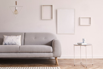 Minimalistic scandinavian interior with design sofa, coffee table, pillow and mock up photo frames. White background walls and modern triangle lamp. Stylish interior of living room. Real photo.