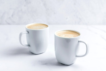 Minimal desk top with two white cups of coffee on marble table. Close-up.