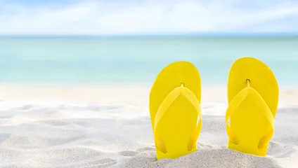 Poster Yellow flip flops on beach sand texture and tropical sea background. Summer holidays and hot season. Fun ocean weekend. Summertime. Selective focus. Banner © ladyalex