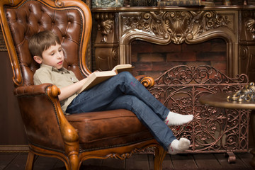 The child in the chair reading a book.Little boy with a book