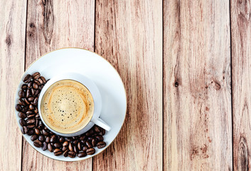 Top view of a cup of hot coffee on wooden rustic table with spilled coffee beans.