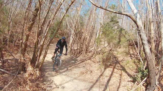 An extreme MTB mountain biker rides tight turns and berms on trails in a forest full of trees and bushes.