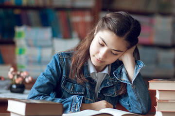 beautiful schoolgirl sitting in the library and reading a book