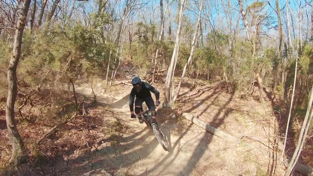 An extreme MTB mountain biker rides tight turns and berms on trails behind a friend very fast in a forest.