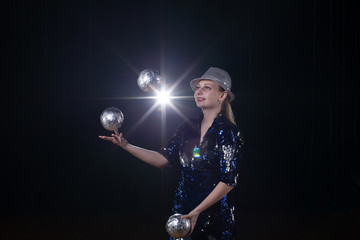 Circus actress performs. The girl juggles balls on a dark background in the spotlights.