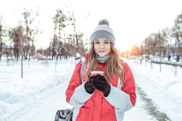 Beautiful girl in a red jacket in winter on the street, on vacation, in the New Year holidays. Happy smiling, holding a cup with a hot drink in his hands, coffee tea, warming.