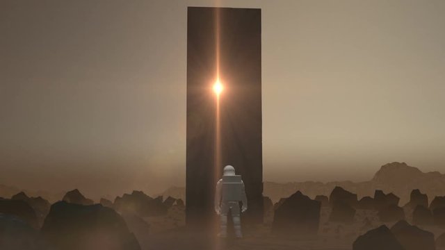 Astronaut walking on the surface of a Mars like planet stops and a Monolith constructs itself in front of him with a light emanating from it.