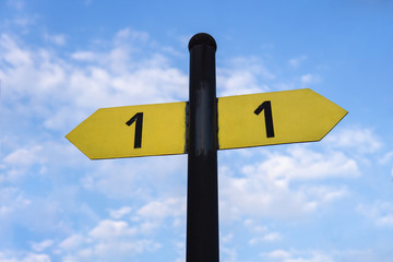 Yellow direction sign on the pole against the blue sky. Yellow arrow signal against sky.