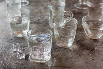 Many glasses of water splashed with drops and pieces of ice on a gray table