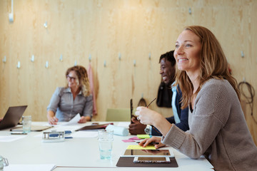 Smiling businesswoman looking away while sitting with colleagues at conference table in board room