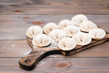 Raw dumplings ready for cooking lie in rows on a wooden cutting board on the table