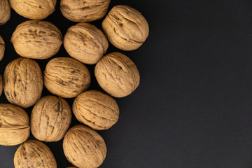 Walnuts in shell lying on black surface, top view. Background of round walnuts. Healthy nuts and seeds composition.