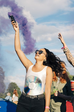 Cheerful woman holding distress flare with purple smoke while enjoying music concert with friends
