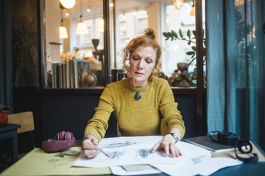 Confident mature female illustrator drawing on paper at desk in creative office