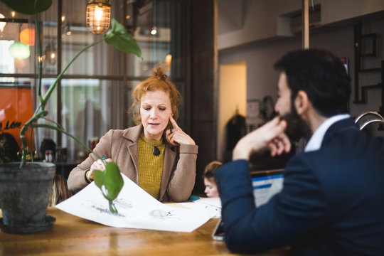 Confident female and male graphic designers discussing over drawing on paper at table in office