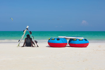 Vertical back view of a man in shade of boards sitting down facing the ocean.