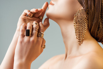 cropped view of young naked woman in golden rings and earrings in turban touching face isolated on...