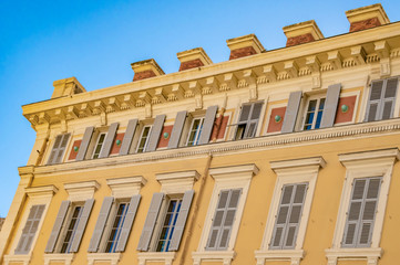 Fototapeta na wymiar View to the decorated facade of a historic house in Nice, France. You can see the typical windows and shutters of a Mediterranean cityscape.