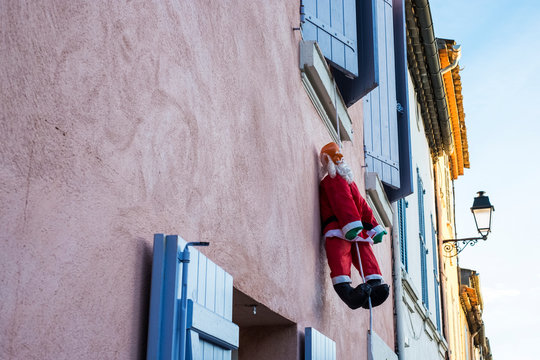 Santa Clause figure hanging on rope from a window of house with pink facade.