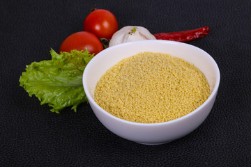Raw couscous in the bowl served salad leaves, tomato and pepper