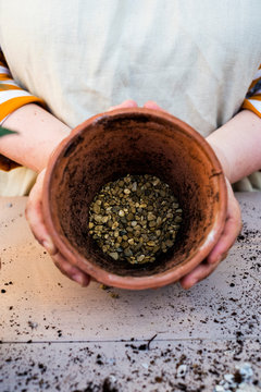 High angle close up of person holding terracotta plant pot with gravel.