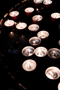 High angle close up of lit tea light candles on a tray in a church.