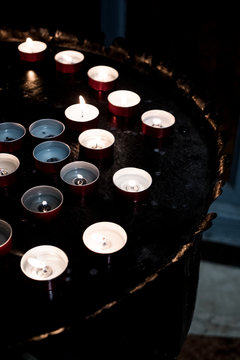 High angle close up of lit tea light candles on a tray in a church.