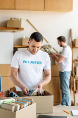 selective focus of handsome volunteer unpacking carton box with footwear