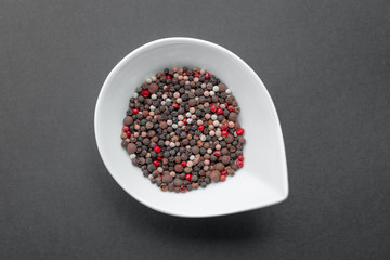 White bowl with colourful peppercorns on blackbackground. Top view, flat lay. Copy space. Natural light. Horizontal image.