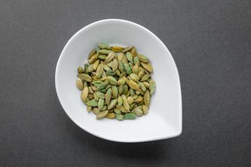 White bowl with cardamon on blackbackground. Top view, flat lay. Copy space. Natural light. Horizontal image. 