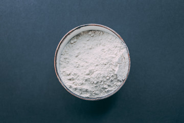 Round bowl full of white flour on black background. Top view, flat lay. Natural light. Copy space.