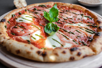 Close up Pizza Margherita with green salsa and leaf of basyl on wooden plate. Black background, top view, flat lay, vertical image. Natural light. Horizontal image.