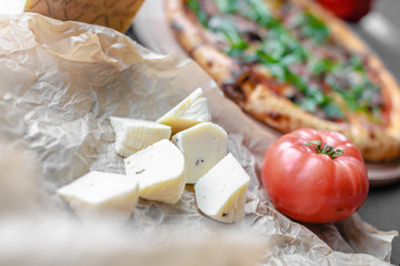 Cheese pieces with fried half of garlic and tomato on white cooking paper with italian pizza with arugula on it. Black background, flat lay, vertical orientation, copy space.