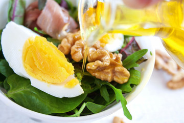 Pour olive oil over a salad with egg, parma ham and walnuts
