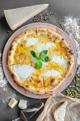 Pizza with four kinds of cheese on the table in the restaurant. Next to spices and different cheese. Vertical image. Natural light. Black background. Top view, flat lay.