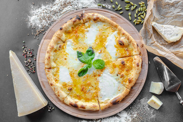 Pizza with four kinds of cheese on the table in the restaurant. Next to spices and different cheese. Horizonal image. Natural light. Black background. Top view, flat lay.