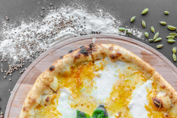 Pizza with four kinds of cheese on the wooden table in the restaurant. Different spices near. Horizonal image. Natural light. Black background. Top view, flat lay.